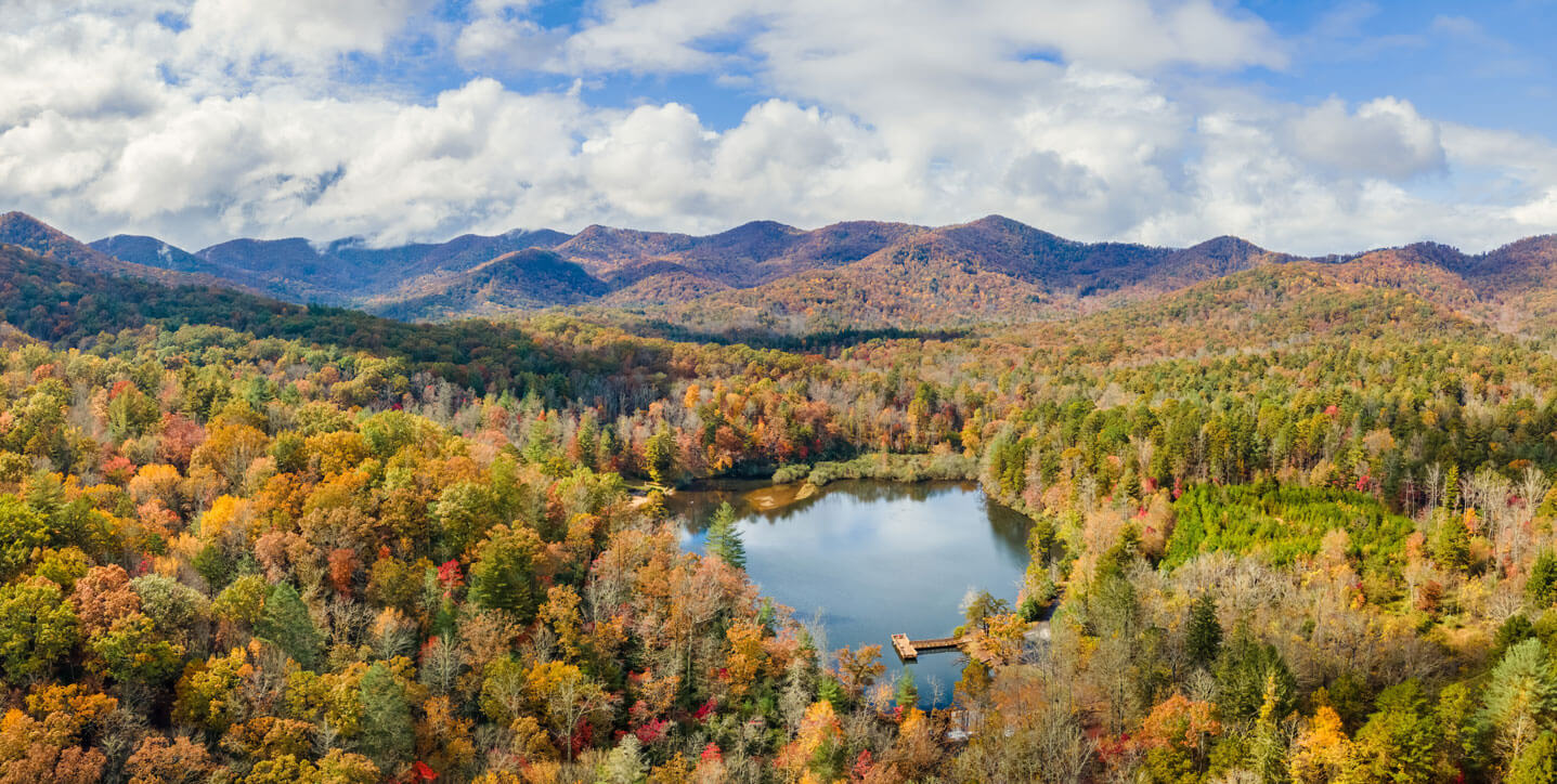 Autumn colored, tree covered hills and a small pond with a pier in North Carolina