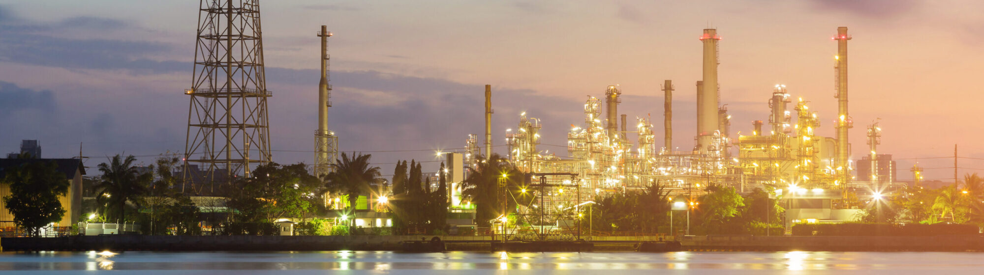 Chemical plant at sunset with water in the foreground, showcasing industrial equipment and structures.
