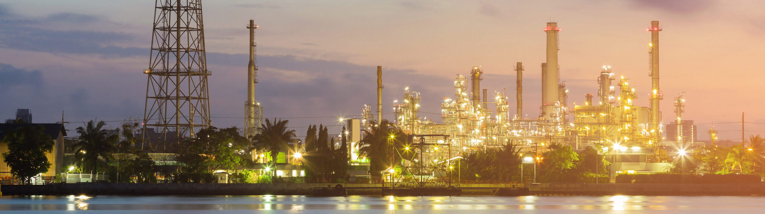 Chemical plant at sunset with water in the foreground, showcasing industrial equipment and structures.