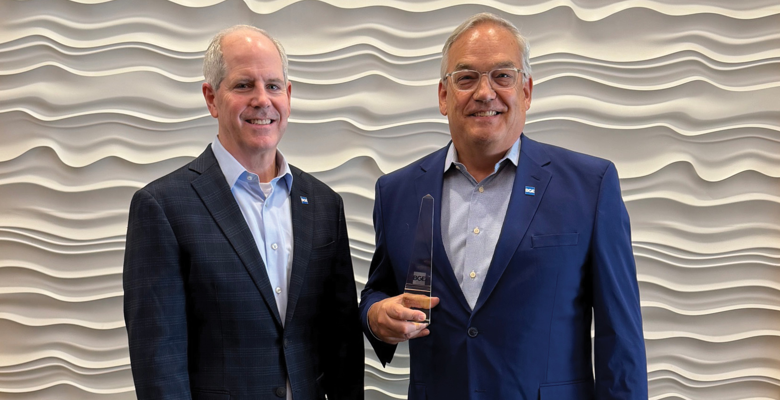 Two men in suits stand smiling. One, David Retzch, holds a clear glass award next to Mike Garrison.